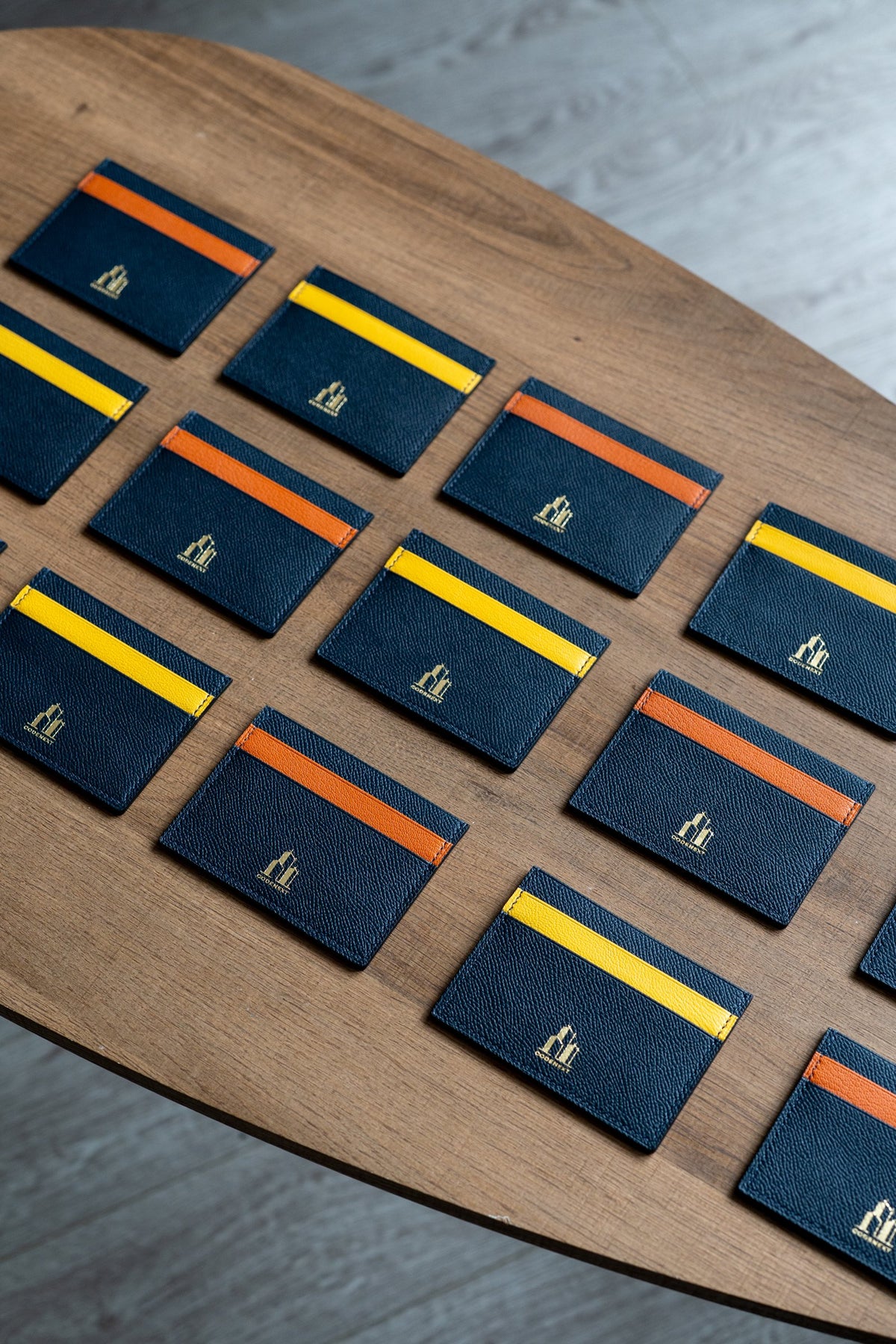 Handmade navy leather card holders with orange and yellow accents and gold foil CODENEXT logo, corporate employee gift
