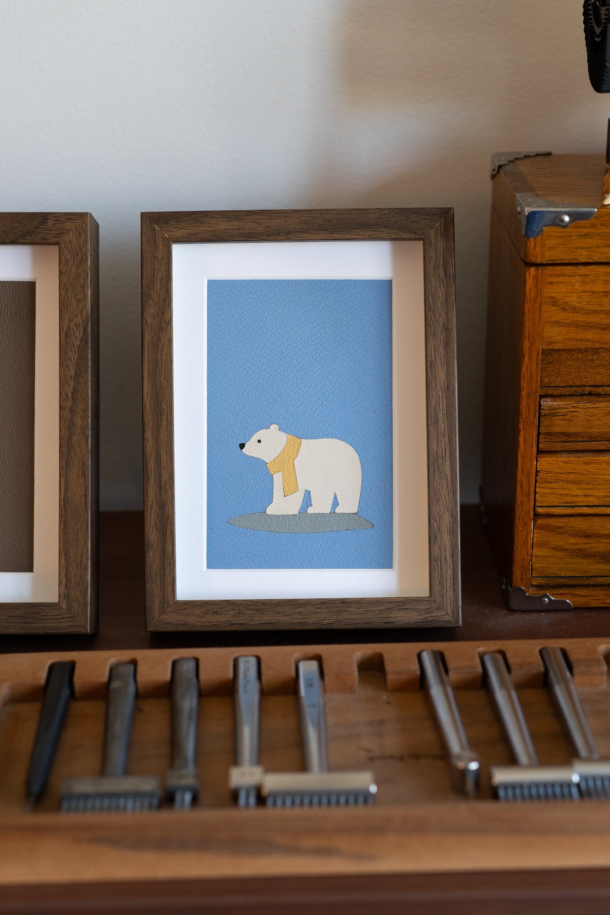 Polar Bear leather art in a walnut frame, a white bear in a yellow scarf on blue leather