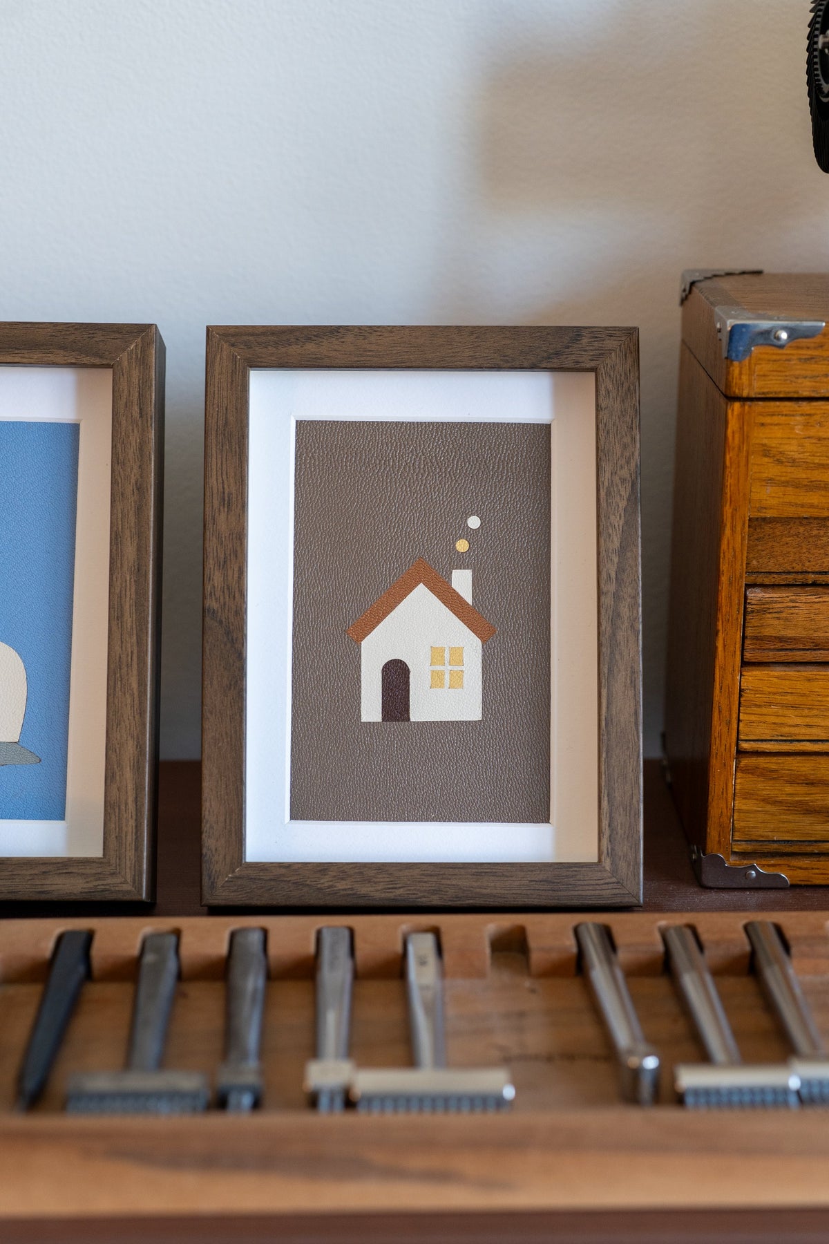Warm Home leather art in a walnut frame, a white house with a brown roof on taupe leather